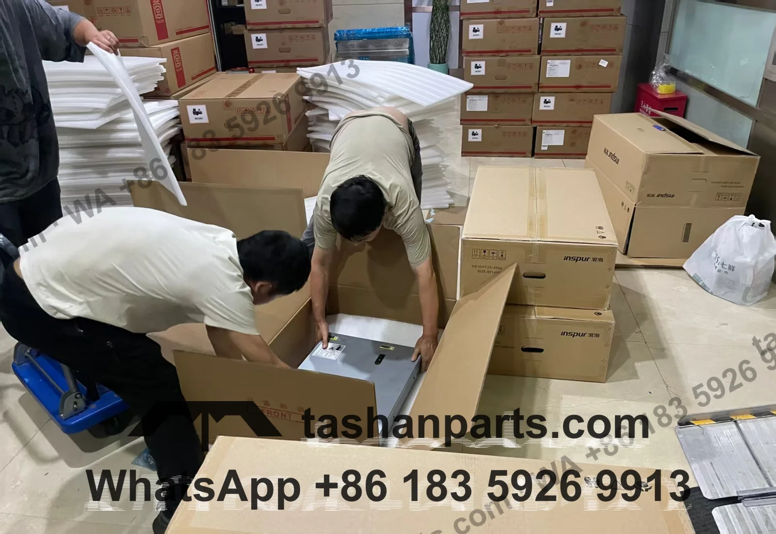 Two workers lowering a server into a carton lined with foam sheets, stacked cartons and foam behind them